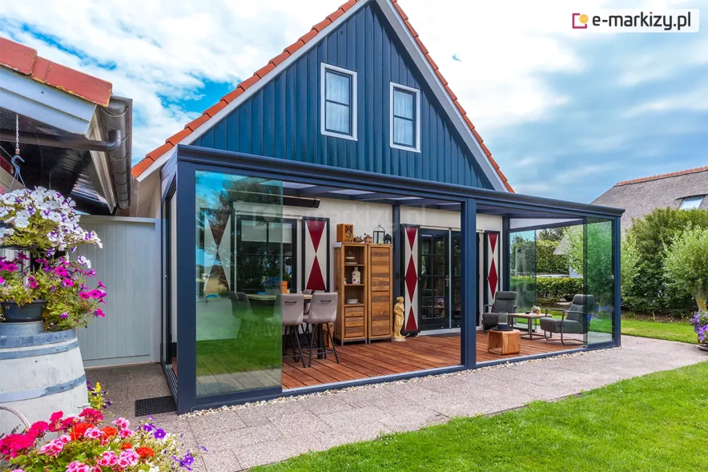 Domek z kopertowym dachem i tarasem drewnianym zabudowanym pergolą aluminiową Lunaro z dachem z płyt poliwęglanowym i otwartymi na oścież przesuwnymi drzwiami szklanymi