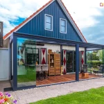 Domek z kopertowym dachem i tarasem drewnianym zabudowanym pergolą aluminiową Lunaro z dachem z płyt poliwęglanowym i otwartymi na oścież przesuwnymi drzwiami szklanymi