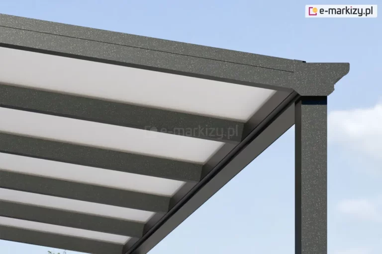 Zbliżenie na górny narożnik nowoczesnego zadaszenia tarasowego w kolorze antracytowym o strukturze drobnoziarnistej. Widoczny jest profil czołowy zintegrowany z systemem rynnowym, zakończony ozdobną, klasyczną maskownicą rynny. Aluminiowa konstrukcja wspiera połacie dachu wykonane z mlecznego poliwęglanu, które są osadzone na równolegle rozmieszczonych krokwiach o prostokątnym przekroju. Całość opiera się na pionowym słupie nośnym, również w kolorze antracytowym. Tło zdjęcia stanowi jasne, lekko zachmurzone niebo, co podkreśla techniczną precyzję detali wykończeniowych systemu.