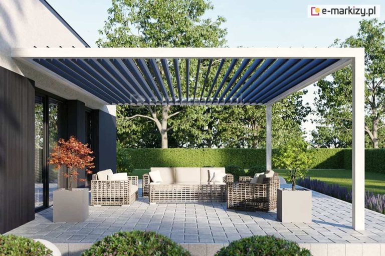 Nowoczesny taras z białą konstrukcją pergoli mocowanej do ściany, uzupełnioną o dach lamelowy Selt SB400 MD. Konstrukcja pergoli, składająca się z ramy i pionowych podpór, wykonana jest z aluminium w kolorze białym, co kontrastuje z ciemnoantracytowymi lamelami dachu. Ruchome pióra są ustawione w pozycji otwartej, prostopadle do podłoża, ukazując rytmiczną strukturę zadaszenia i pozwalając na swobodny przepływ światła. Pod pergolą zaaranżowano strefę wypoczynkową z technorattanowymi meblami w jasnym kolorze, w tym dużą sofą i fotelami z miękkimi poduszkami. Nawierzchnia tarasu wyłożona jest jasnoszarą kostką brukową, a na jej obrzeżach ustawiono minimalistyczne, betonowe donice z ozdobnymi roślinami. W tle widoczny jest zadbany, zielony ogród z wysokim żywopłotem oraz dużymi drzewami liściastymi. Nowoczesna bryła budynku z dużymi przeszkleniami i ciemną elewacją dopełnia kompozycję, tworząc spójną przestrzeń rekreacyjną.