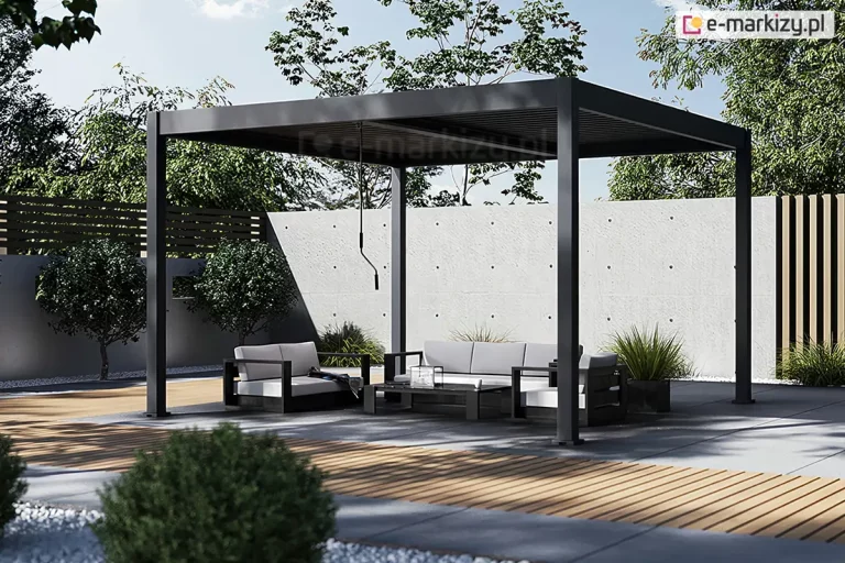 Pergola metalowa Marlo Duo o konstrukcji aluminiowej w kolorze ciemnego grafitu umieszczona w minimalistycznie zaaranżowanym ogrodzie. Konstrukcja pergoli opiera się na czterech solidnych pionowych słupach o kwadratowym przekroju, które podtrzymują płaski dach wyposażony w ruchome lamele pozwalające na regulację dopływu światła słonecznego. Pod zadaszeniem znajduje się zestaw mebli ogrodowych składający się z trzyosobowej sofy, fotela oraz niskiego prostokątnego stolika kawowego. Meble mają czarne ramy i jasnoszare, kontrastujące poduszki siedziskowe oraz oparciowe. Na stoliku widoczne są drobne akcesoria dekoracyjne. Podłoże pod pergolą oraz w jej bezpośrednim sąsiedztwie wykonane jest z dużych, gładkich płyt betonowych w jasnym odcieniu szarości, które przeplatają się z pasami drewnianego podestu o ciepłej barwie. W tle widoczne jest ogrodzenie wykonane z surowego betonu architektonicznego z regularnie rozmieszczonymi otworami technologicznymi, a za nim rosną wysokie liściaste drzewa oraz ozdobne krzewy. Po lewej stronie kompozycji znajdują się dwa przycięte w kulę krzewy posadzone w pasie wysypanym białym grysem, natomiast po prawej stronie widać fragment pionowych drewnianych lameli stanowiących element dekoracyjny ogrodzenia oraz kępy ozdobnych traw. Całość sceny jest oświetlona naturalnym, dziennym światłem, które rzuca wyraźne, geometryczne cienie na nawierzchnię tarasu.