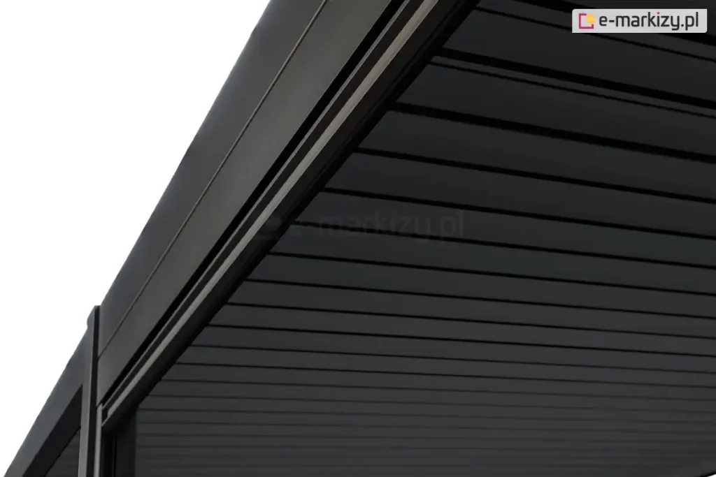 Zbliżenie na narożnik górnej konstrukcji pergoli Gloria w kolorze ciemnoantracytowym, przedstawiające detal prowadnicy i zadaszenia. Zdjęcie wykonane z perspektywy od dołu ukazuje solidną, aluminiową ramę o matowym wykończeniu z precyzyjnie wyprofilowanym wgłębieniem, w którym osadzona jest roleta lub system uszczelniający. Zadaszenie składa się z równolegle ułożonych, płaskich lameli o gładkiej strukturze, które są ciasno dopasowane, tworząc szczelną i jednolitą płaszczyznę w ciemnym odcieniu. W lewym dolnym rogu widoczny jest fragment pionowego słupa nośnego, który łączy się z belką dachową pod kątem prostym, podkreślając nowoczesny i minimalistyczny charakter zabudowy.