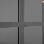 Zbliżenie na detale konstrukcyjne przesuwnych drzwi poliwęglanowych do pergoli Gloria w kolorze ciemnoantracytowym. Zdjęcie koncentruje się na pionowym profilu ramy, który stanowi punkt styku dwóch paneli, oraz na poziomych szprosach wzmacniających, dzielących płaszczyznę drzwi na mniejsze sekcje. Wypełnienie skrzydeł drzwiowych stanowi półprzezroczysty, przydymiony poliwęglan, który delikatnie rozprasza światło, zapewniając prywatność przy jednoczesnym zachowaniu widoczności zarysów otoczenia. Wszystkie elementy aluminiowe charakteryzują się gładkim, matowym wykończeniem i precyzyjnym dopasowaniem krawędzi, co podkreśla nowoczesną estetykę systemu zabudowy.