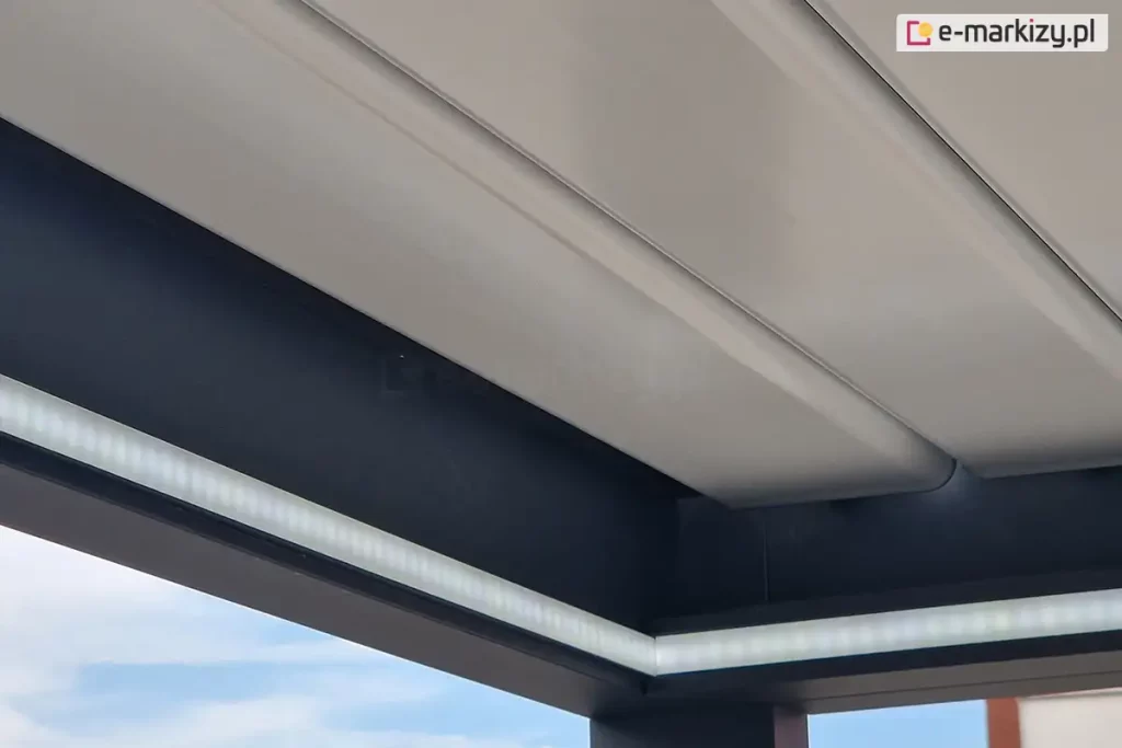 Belki zwieńczenia pergoli z zamontowanym oświetleniem led w formie taśmy pod złożonym dachem z białych lameli aluminiowych