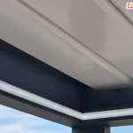 Belki zwieńczenia pergoli z zamontowanym oświetleniem led w formie taśmy pod złożonym dachem z białych lameli aluminiowych