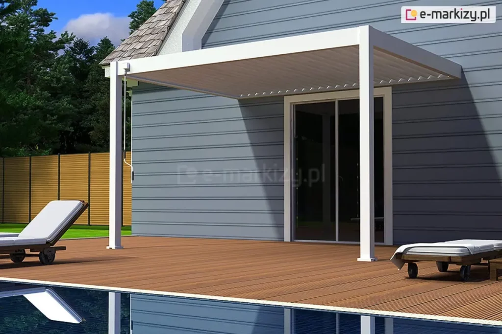 Biała pergola tarasowa Marlo zamontowana do elewacji klasycznego budynku z szarymi panelami ściennymi. Konstrukcja pergoli opiera się na dwóch pionowych, kwadratowych słupach wspierających zadaszenie z ruchomymi lamelami ustawionymi w pozycji zamkniętej. Pergola osłania wyjście tarasowe z przesuwnymi przeszklonymi drzwiami. Całość znajduje się na drewnianym tarasie wykonanym z brązowych desek kompozytowych, umiejscowionym bezpośrednio przy basenie, którego fragment tafli wody widoczny jest na pierwszym planie. Po lewej i prawej stronie na tarasie ustawione są nowoczesne leżaki basenowe z białymi materacami. W tle widoczne jest zielone ogrodzenie panelowe oraz ściana drzew iglastych pod jasnoniebieskim, lekko zachmurzonym niebem.