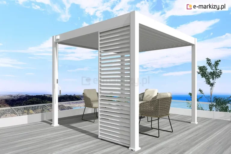 Biała wolnostojąca pergola lamelowa Marlo o kwadratowej podstawie, zamontowana na tarasie z widokiem na morze. Konstrukcja zadaszenia posiada dach z ruchomych lamel ustawionych w pozycji całkowicie zamkniętej oraz pionowy, biały panel żaluzjowy zamontowany w jednym z narożników, który służy jako przesłona boczna. Przy słupie nośnym po lewej stronie widoczny jest mechanizm korbowy do ręcznego sterowania kątem nachylenia lamel dachowych. Pod pergolą, na podłożu z jasnoszarych desek tarasowych, ustawiono dwa nowoczesne fotele z ażurowym splotem i jasnymi poduszkami. Taras zabezpieczony jest niską, białą barierką z przeszkleniami, za którą rozpościera się widok na wybrzeże i błękitną wodę pod jasnym niebem z delikatnymi chmurami.