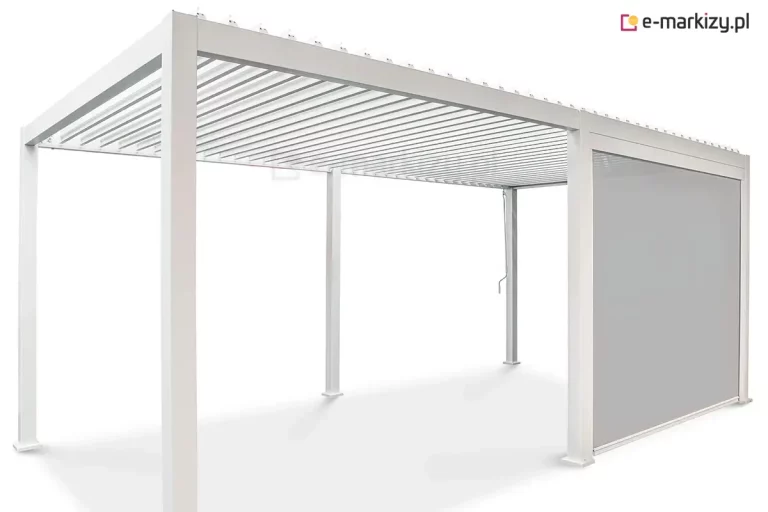 Wolnostojąca pergola bioklimatyczna Gloria o konstrukcji modułowej wykonana z aluminium w kolorze białym przedstawiona na jednolitym jasnym tle. Produkt składa się z dwóch połączonych segmentów wspartych na sześciu pionowych słupach o kwadratowym przekroju z widocznymi stopami montażowymi. Zadaszenie tworzy system poziomych ruchomych lameli aluminiowych w kolorze białym, które są ustawione w pozycji otwartej. Jeden z bocznych modułów pergoli został wyposażony w zintegrowaną roletę pionową typu screen w kolorze jasnoszarym, która jest całkowicie rozwinięta i osłania przestrzeń między dwoma słupami. Przy jednym ze słupów widoczna jest metalowa korba służąca do manualnej regulacji kąta nachylenia lameli dachowych. Całość konstrukcji charakteryzuje się minimalistycznym, nowoczesnym designem z ukrytymi systemami odprowadzania wody wewnątrz profili.