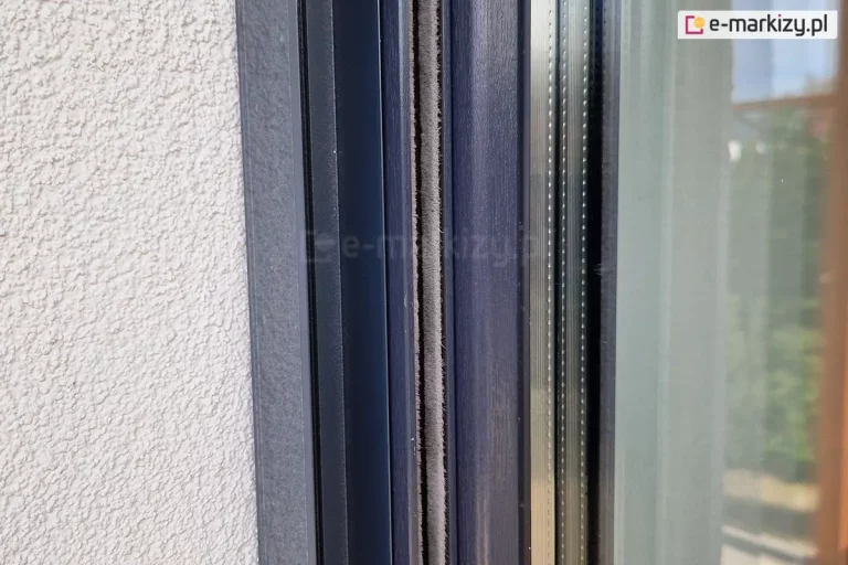 Profil boczny moskitiery plisowanej zamocowanej do prowadnic rolety zewnętrznej oraz ramy okna. Wszystkie elementy wykonano w kolorze antracytowym.