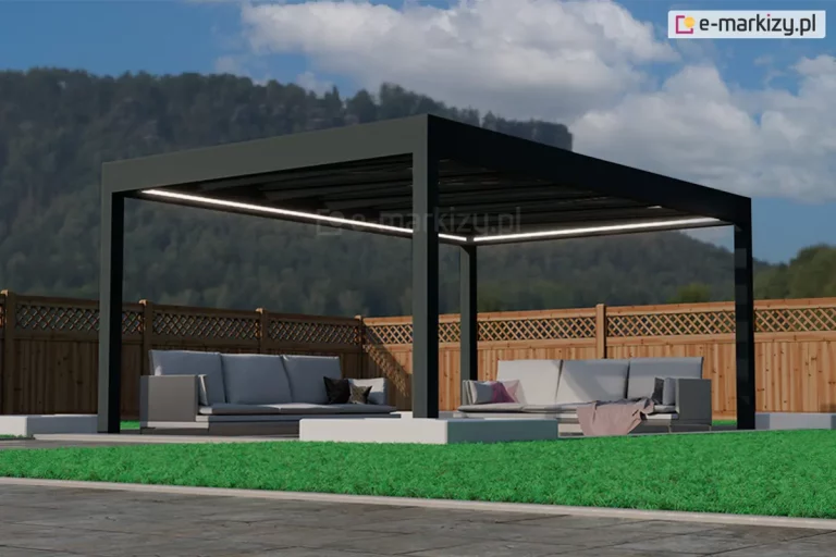 Wolnostojąca altana ogrodowa Spekta Glass o geometrycznej konstrukcji wykonanej z profili aluminiowych w kolorze głębokiej czerni. Rama nośna opiera się na czterech masywnych słupach o przekroju kwadratowym, a jej płaski dach posiada wypełnienie z dużych tafli szkła, które zapewniają ochronę przed opadami bez ograniczania dopływu światła. Wzdłuż wewnętrznych krawędzi konstrukcji zainstalowano system liniowego oświetlenia LED, emitujący ciągły pas intensywnego, białego światła. Pod zadaszeniem zorganizowano strefę wypoczynkową z dwiema dużymi sofami ogrodowymi w kolorze jasnoszarym, wyposażonymi w miękkie poduchy oraz dekoracyjny, różowy koc. Podłoże pod altaną stanowią gładkie, jasnoszare płyty tarasowe, które kontrastują z otaczającym je żywozielonym, krótko przystrzyżonym trawnikiem. W bezpośrednim sąsiedztwie słupów wkomponowano niskie, białe donice o geometrycznym kształcie, wypełnione drobnym, jasnym kruszywem. Tło kompozycji stanowi wysokie, drewniane ogrodzenie panelowe z ozdobnym, ażurowym wykończeniem w górnej części, za którym rozciąga się widok na zalesione wzgórze pod błękitnym niebem. Całość realizacji charakteryzuje się nowoczesnym designem i wysoką estetyką, tworząc luksusowe miejsce do rekreacji.