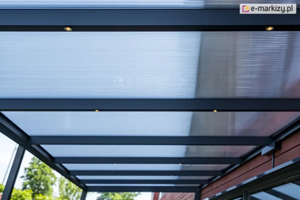 Dach zadaszenia z poliwęglanu Lunaro Bosco Deponti wykonany z antracytowej konstrukcji oraz wypełnienia z poliwęglanu komorowego z widocznymi w belkach krokwiowych punktami oświetlenia LED.