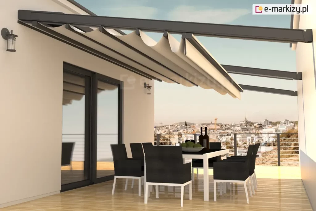 Nowoczesny dach rzymski Square zamontowany na przestronnym tarasie apartamentu. Konstrukcja zadaszenia opiera się na solidnych, aluminiowych profilach w kolorze antracytowym, które są przytwierdzone do elewacji budynku i wsparte na poprzecznych belkach. Jasnobeżowa, wodoodporna tkanina jest częściowo rozwinięta, tworząc charakterystyczne, głębokie fałdy podwieszone pod prowadnicami. Pod zadaszeniem znajduje się strefa jadalniana z dużym białym stołem oraz kompletem ośmiu nowoczesnych krzeseł w kolorze czarnym z białymi nogami. Taras wykończony jest jasnymi deskami kompozytowymi o wysokim połysku, w których odbijają się meble i elementy konstrukcyjne. W tle rozpościera się szeroka panorama miasta widoczna z dużej wysokości, ograniczona minimalistyczną balustradą ze stalowych linek. Na ścianie budynku, obok dużych przeszkleń, zamontowane są klasyczne kinkiety zewnętrzne, a całość oświetlona jest ciepłym światłem zachodzącego słońca, co podkreśla ekskluzywny charakter aranżacji.