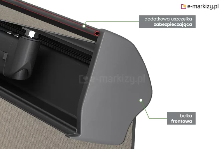Zdjęcie produktowe wykonane w zbliżeniu typu makro przedstawia detal konstrukcyjny, jakim jest dodatkowa uszczelka w belce przedniej markizy Dakar. Na jasnym tle widoczny jest profil czołowy w kolorze antracytowym o matowym wykończeniu i charakterystycznym, opływowym kształcie. W górnej części profilu, w specjalnie wyprofilowanym rowku, umieszczona jest czarna uszczelka, która przylega bezpośrednio do tkaniny poszycia w kolorze jasnoszarym. Precyzyjne ujęcie pokazuje sposób, w jaki uszczelka domyka przestrzeń między materiałem a profilem, co w markizie Dakar służy zabezpieczeniu wnętrza kasety przed zanieczyszczeniami i wilgocią po całkowitym zwinięciu urządzenia. Fotografia ma charakter techniczny, podkreślając wysoką jakość wykończenia i dbałość o detale mechanizmu ochronnego.