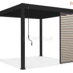 Grafika przedstawia trójwymiarową wizualizację nowoczesnej pergoli ogrodowej w kolorze czarnym lub ciemnoantracytowym, zaprezentowaną na białym, neutralnym tle. Konstrukcja wsparta jest na czterech masywnych, kwadratowych słupach nośnych, a jej zadaszenie składa się z gęsto rozmieszczonych, czarnych lameli. Głównym elementem funkcjonalnym pokazanym na zdjęciu jest jeden przesuwny panel boczny zamontowany w świetle prawego boku pergoli. Panel ten posiada czarną ramę, która została wypełniona poziomymi lamelami w kolorze jasnego drewna, co tworzy kontrastowy i dekoracyjny efekt wizualny. Lamele w panelu są ustawione pod stałym kątem, tworząc strukturę przypominającą żaluzje. Przy lewym przednim słupie pergoli zamontowany jest długi, czarny drążek korbowy, służący do ręcznej obsługi mechanizmów konstrukcji. Całość ukazana jest w ujęciu perspektywicznym, pozwalającym na dokładne przyjrzenie się detalom łączeń profili oraz strukturze wypełnienia panelu bocznego.