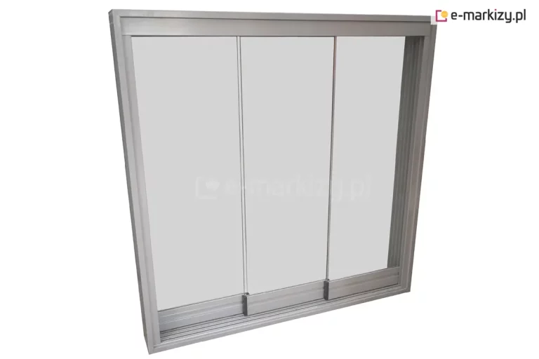 Szklane ściany przesuwne Miros przedstawione na zdjęciu to nowoczesny system zabudowy składający się z trzech bezramowych paneli szklanych umieszczonych w solidnej konstrukcji aluminiowej w kolorze srebrnym lub anodowanym. Każdy z trzech modułów szklanych jest osadzony w dolnej prowadnicy za pomocą poziomych profili jezdnych, które zapewniają stabilność i płynność ruchu podczas otwierania i zamykania segmentów. Całość zamknięta jest w szerokiej ramie obwodowej z widocznymi wielotorowymi prowadnicami dolnymi i górnymi, co pozwala na kaskadowe przesuwanie się tafli szkła jedna za drugą. Konstrukcja charakteryzuje się minimalistycznym designem, w którym pionowe krawędzie szkła pozbawione są szerokich profili, co maksymalizuje przejrzystość i widoczność. Dolna szyna posiada wyraźnie zaznaczone tory jezdne, a precyzyjne spasowanie elementów gwarantuje szczelność i estetyczny wygląd systemu dedykowanego do zabudowy tarasów, balkonów lub pergoli.