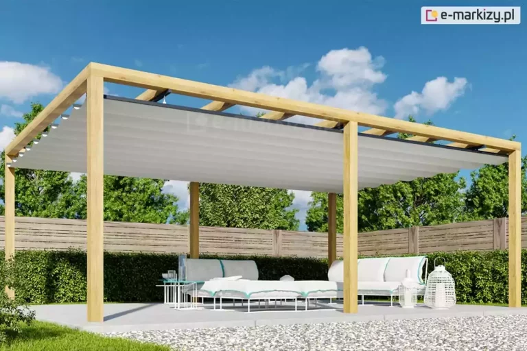 Duża pergola drewniana Juko wolnostojąca ustawiona w ogrodzie w pobliżu drewnianego ogrodzenia oraz niskiego żywopłotu. Konstrukcja na 6 podporach wyposażona w opcjonalny dach rzymski osłania przed słońcem białe meble ogrodowe ustawione na płycie tarasu.