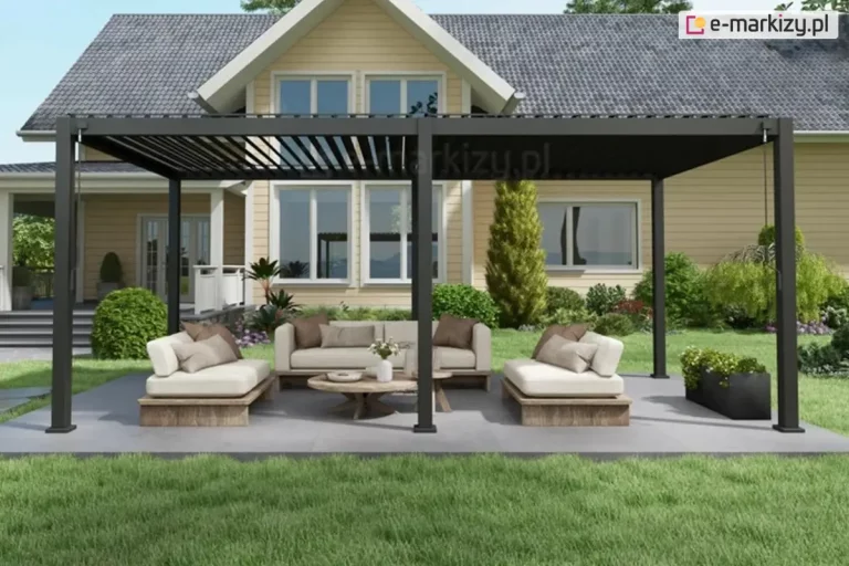Czarna, wolnostojąca pergola tarasowa Gloria o konstrukcji aluminiowej z otwieranym dachem lamelowym, ustawiona na szarej płycie tarasowej w ogrodzie. Pod pergolą znajduje się zestaw mebli wypoczynkowych składający się z trzyosobowej sofy oraz dwóch szezlongów w kolorze beżowym z brązowymi poduszkami, ustawionych wokół niskiego, okrągłego stolika kawowego z drewna. Konstrukcja pergoli oparta jest na sześciu pionowych słupach, a zadaszenie tworzą ruchome, poziome lamele ustawione pod kątem, wpuszczające światło słoneczne. W tle widoczny jest piętrowy dom jednorodzinny o żółtej elewacji z białymi obramowaniami okien oraz zadbany trawnik z krzewami ozdobnymi, w tym żywotnikiem (tują) i roślinami płożącymi. Po prawej stronie przy pergoli stoi czarna, podłużna donica z niską roślinnością.
