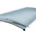 Zdjęcie prezentuje wielkoformatowe zadaszenie drzwiowe Elegant XL w wersji kolorystycznej jasnoniebieskiej o satynowym wykończeniu. Konstrukcja charakteryzuje się szeroką, łukowatą taflą wypełnienia, która dzięki matowej strukturze delikatnie rozprasza światło, zachowując jednocześnie błękitny odcień. Płyta jest stabilizowana przez system punktowych uchwytów oraz osadzona na srebrnych, metalowych wspornikach o ażurowym profilu. Przednia krawędź daszka została wyposażona w aluminiową rynnę odpływową o okrągłym przekroju, zakończoną czarnymi elementami maskującymi. Wzdłuż tylnej krawędzi przebiega sztywna listwa montażowa, ułatwiająca szczelne połączenie z elewacją budynku. Produkt przedstawiony jest w perspektywie, która podkreśla jego dużą rozpiętość oraz nowoczesną, techniczną estetykę.