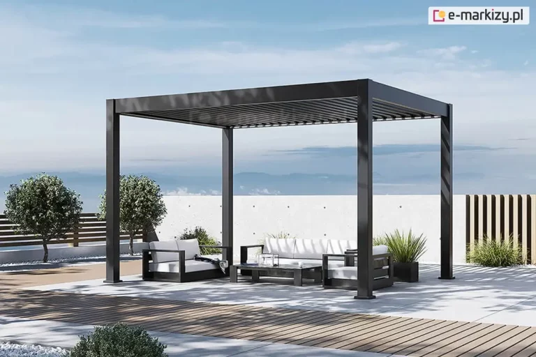 Wizualizacja wolnostojącej pergoli bioklimatycznej Rubio w kolorze antracytowym, zainstalowanej na nowoczesnym tarasie widokowym. Konstrukcja wsparta na czterech masywnych słupach o kwadratowym przekroju, z dachem wykonanym z ruchomych lameli aluminiowych ustawionych w pozycji zamkniętej. Pod pergolą znajduje się strefa wypoczynkowa z luksusowymi meblami ogrodowymi: niską sofą, fotelami z białymi poduszkami oraz minimalistycznym stolikiem kawowym. Podłoże tarasu wykończone jasnoszarymi płytami betonowymi, które przechodzą w pasy z brązowej deski kompozytowej. W tle widoczna jest niska, biała ściana oporowa z surowego betonu, za którą rozpościera się szeroka panorama z widokiem na zamglone pasma górskie pod jasnym, błękitnym niebem. Aranżację uzupełnia starannie dobrana roślinność: formowane krzewy w ozdobnym grysie oraz wysokie trawy w czarnych, geometrycznych donicach. Całość prezentuje luksusową przestrzeń rekreacyjną zaprojektowaną w stylu minimalistycznym.