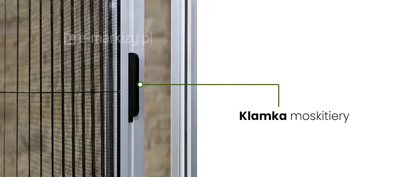 Zdjęcie przedstawia zbliżenie na pionowy profil aluminiowy moskitiery Zig-Zag w kolorze białym lub jasnoszarym, w którym zamontowano ergonomiczną klamkę do obsługi systemu przesuwnego. Klamka moskitiery ma formę podłużnego, wąskiego uchwytu wykonanego z czarnego tworzywa, który jest wpuszczony w ramę prowadzącą. Od klamki odchodzi zielona linia pomocnicza zakończona białym punktem, wskazująca na element i prowadząca do napisu w języku polskim Klamka moskitiery umieszczonego na białym tle po prawej stronie grafiki. Po lewej stronie widoczny jest fragment napiętej siatki plisowanej w ciemnym kolorze, która charakteryzuje się regularnymi, pionowymi zagięciami typowymi dla modelu moskitiera Zig-Zag. Siatka jest zintegrowana z aluminiową konstrukcją, a w tle widać rozmyty zarys elewacji budynku lub wnęki okiennej. Całość kompozycji ma charakter instruktażowy i techniczny, skupiając się na detalach wykończenia osłony przeciw owadom.