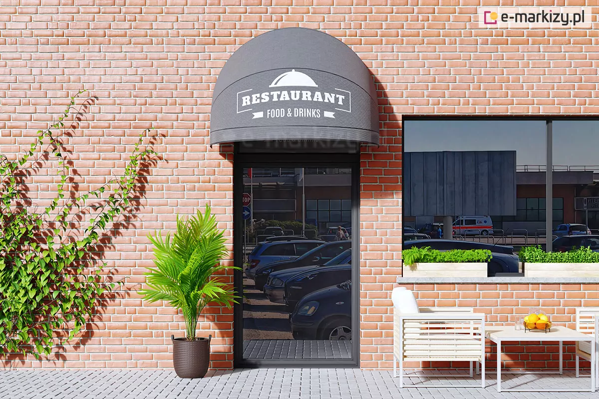 Zdjęcie przedstawia wizualizację nowoczesnej markizy koszowej o półkolistym kształcie, zamontowanej nad przeszklonymi drzwiami wejściowymi do lokalu gastronomicznego. Poszycie markizy wykonane jest z gładkiego materiału w kolorze ciemnoszarym, na którym umieszczono białą grafikę z napisem „RESTAURANT FOOD & DRINKS” oraz piktogramem przykrytego talerza serwującego. Markiza jest precyzyjnie dopasowana do szerokości otworu drzwiowego. Elewacja budynku wykonana jest z czerwonej cegły o jasnych fugach. Po lewej stronie drzwi, na ceglanej ścianie, pnie się zielona roślina, a obok, w ciemnobrązowej donicy o plecionej strukturze, rośnie ozdobna palma. Po prawej stronie widoczne jest duże okno z ciemną ramą, w którym odbija się miejska przestrzeń z zaparkowanymi samochodami. Pod oknem znajduje się fragment letniego ogródka z jasnymi meblami o minimalistycznej konstrukcji: białym fotelem z poduszką oraz stolikiem, na którym stoi misa z owocami i szklanka z napojem. Przed wejściem rozciąga się chodnik wyłożony jasnoszarą kostką brukową. Całość sceny jest oświetlona jasnym, dziennym światłem, co tworzy przejrzysty i zapraszający wizerunek nowoczesnej restauracji.