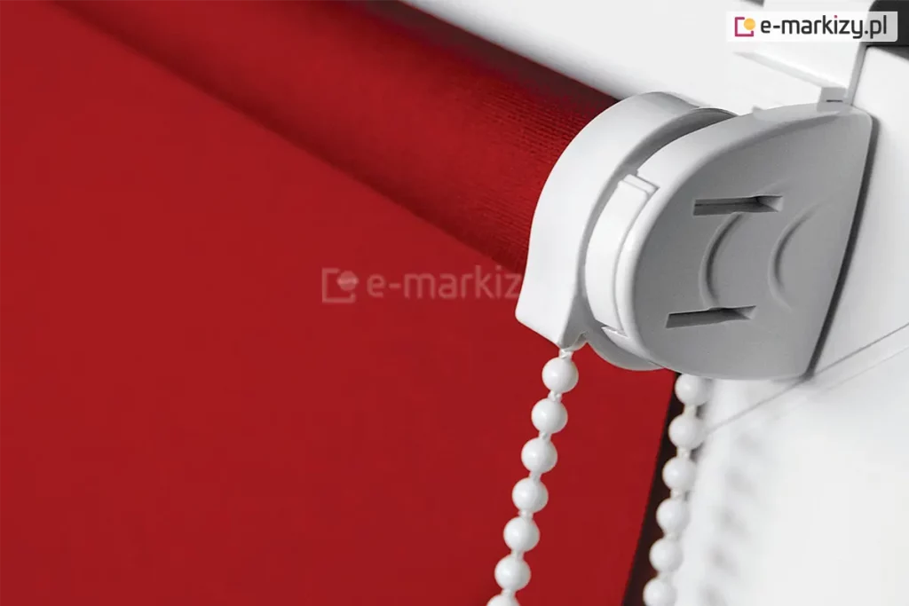 Roletka mini zawieszona na skrzydle okna z białym mechanizmem i soczyście czerwoną tkaniną przeciwsłoneczną.