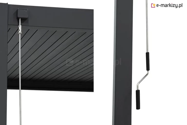 Zbliżenie na mechanizm sterowania korbowego nowoczesnej pergoli tarasowej Gloria w kolorze antracytowym. Po lewej stronie widoczny jest górny detal konstrukcji: kwadratowy przegub zamontowany na ramie, do którego podpięty jest metalowy drążek za pomocą srebrnego zaczepu. W tle widoczne są aluminiowe lamele dachu pergoli. Po prawej stronie zdjęcia, obok słupa pergoli, znajduje się dolna część drążka zakończona wygiętą korbą z dwoma czarnymi, ergonomicznymi uchwytami z tworzywa sztucznego, służąca do ręcznego obracania piór dachu. Całość konstrukcji charakteryzuje się matowym wykończeniem i minimalistycznym designem.