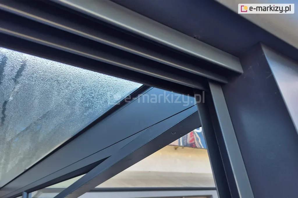 Zbliżenie na połączenie prowadnicy górnej oraz bocznego profilu doszczelniającego U. Całość wykonana w kolorze dopasowanym do kolorystyki zadaszenia ze szkłem.