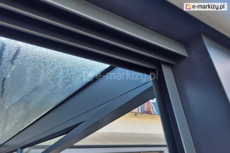 Zbliżenie na połączenie prowadnicy górnej oraz bocznego profilu doszczelniającego U. Całość wykonana w kolorze dopasowanym do kolorystyki zadaszenia ze szkłem.