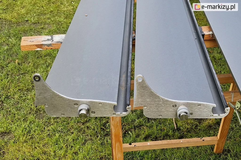 Dwa lamele dachu SB400 MD Selt ułożone na drewnianych wspornikach ustawionych na trawniku. Wyraźnie widoczna budowa lamela w kolorze antracytowym oraz elementy łączące lamele z profilem i mechanizmem sterującym.