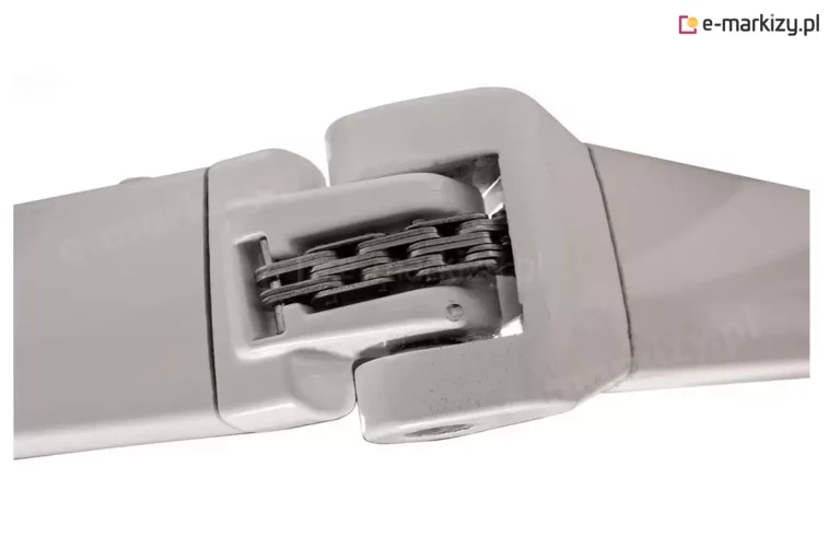 Zbliżenie na aluminiowy przegub ramienia markizy w kolorze białym, przedstawiający mechanizm zgięcia. Centralnym elementem konstrukcji jest wielorzędowy, stalowy łańcuch Flynna (łańcuch płytkowy), który odpowiada za napinanie ramienia. Łańcuch składa się z ciemnych, precyzyjnie połączonych ogniw osadzonych wewnątrz wyprofilowanej wnęki ramienia. Obudowa przegubu wykonana jest z lakierowanego proszkowo aluminium o gładkim wykończeniu, z widocznymi krawędziami odlewu oraz otworem montażowym na dolnej powierzchni sworznia.