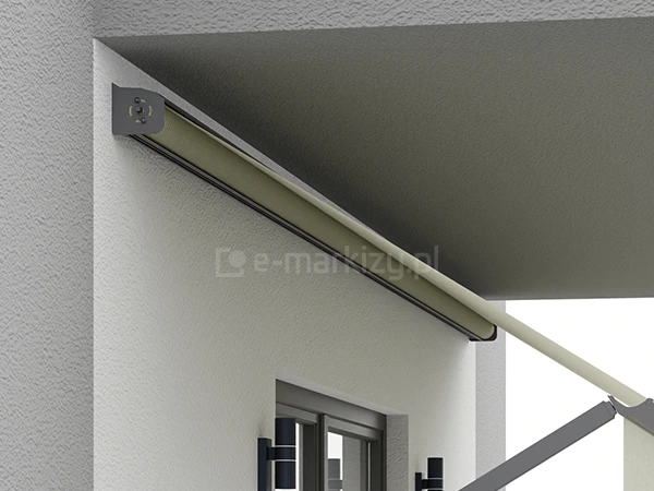 bliżenie na kasetę markizy balkonowej oraz jej mocowanie, zamontowane w narożniku między ścianą a sufitem (płytą balkonową). Aluminiowa kaseta w kolorze antracytowym chroni wał nawojowy z nawiniętą tkaniną w kolorze beżowym. Widoczny jest boczny uchwyt montażowy o profilu litery L, przytwierdzony do białej, tynkowanej elewacji. Z kasety wyprowadzone jest ramię boczne oraz płat materiału, który rozwija się pod skosem. W dolnej części kadru widoczny jest fragment wnęki okiennej z ciemną ramą oraz czarna oprawa oświetleniowa typu kinkiet o cylindrycznym kształcie. Ściana budynku ma wyraźną strukturę tynku typu "baranek".