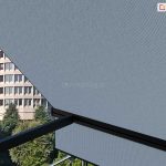 Widok z balkonu lub tarasu na rozwiniętą markizę zewnętrzną Italia wykonaną z tkaniny akrylowej w kolorze jasnoszarym o drobnoziarnistym splotcie. Materiał markizy jest napięty na czarnej, aluminiowej konstrukcji składającej się z poziomej belki dolnej oraz prostopadłych ramion bocznych. W lewej części kadru, za krawędzią poszycia, widoczna jest miejska panorama z charakterystycznym, wysokim budynkiem o cylindrycznym kształcie i jasnej elewacji z gęsto rozmieszczonymi oknami. Poniżej budynku znajdują się korony zielonych drzew liściastych i iglastych, które wypełniają dolną część tła. Całość ujęcia jest oświetlona naturalnym światłem dziennym pod kątem, co uwypukla fakturę materiału markizy oraz tworzy kontrast między zacienioną strefą pod osłoną a jasnym tłem urbanistycznym.