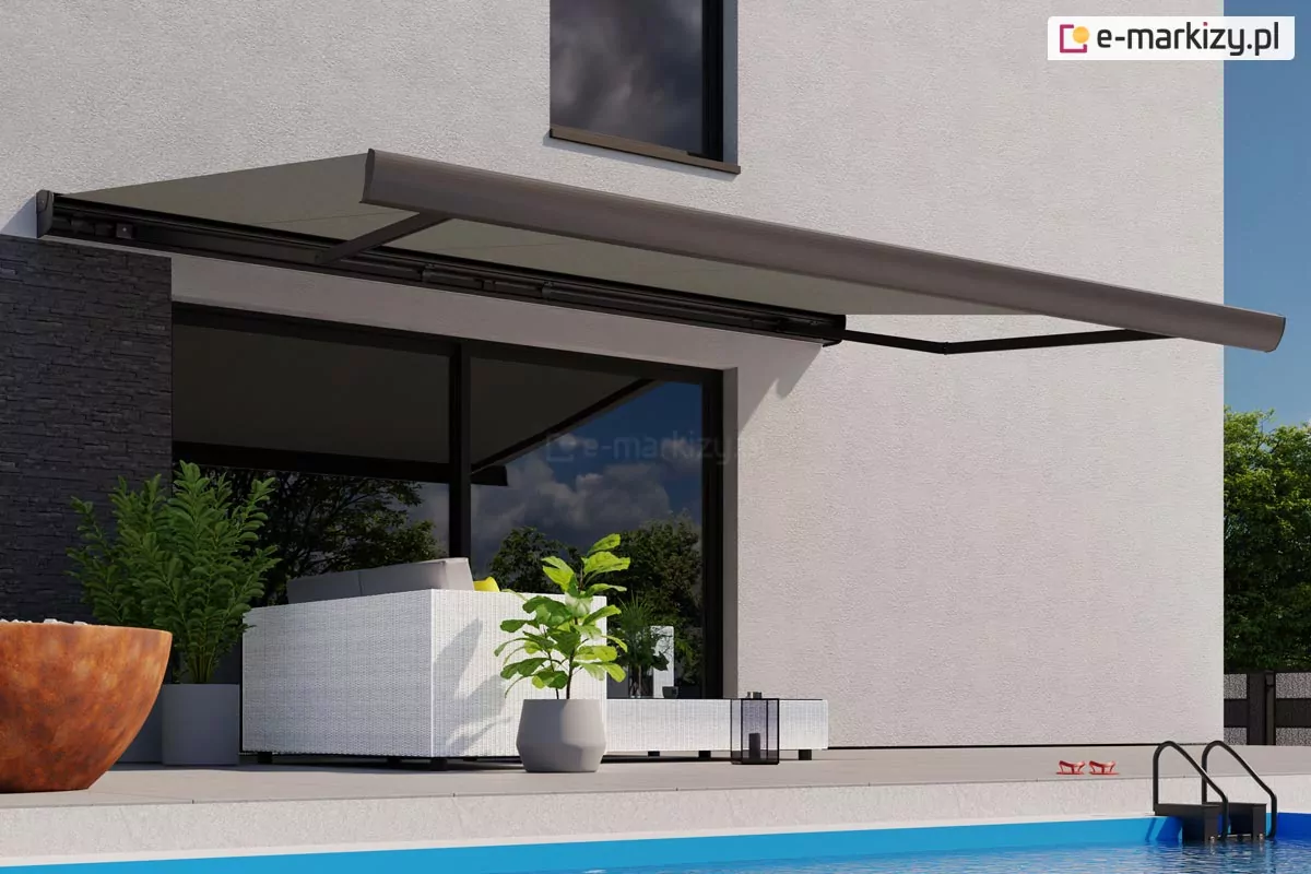 Zdjęcie prezentuje nowoczesną aranżację przydomowej strefy relaksu, w której głównym elementem jest rozłożona markiza Corsica zamontowana na elewacji piętrowego budynku. Markiza posiada poszycie w stonowanym, ciemnoszarym lub antracytowym kolorze, które idealnie komponuje się z czarną konstrukcją ramion oraz kasety. Produkt jest zamontowany nad szerokim przeszkleniem parteru, rzucając wyraźny cień na meble tarasowe i chroniąc wnętrze domu przed bezpośrednim nasłonecznieniem. Elewacja budynku wykonana jest z jasnego, białego tynku o delikatnej strukturze, co tworzy kontrast z ciemnymi detalami stolarki okiennej oraz fragmentem ściany wyłożonym czarnym kamieniem dekoracyjnym po lewej stronie. Pod markizą znajduje się zestaw wypoczynkowy wykonany z białego technorattanu z szarymi poduchami, a obok ustawiono nowoczesne donice z żywą roślinnością, w tym fikus dębolistny oraz inne krzewy ozdobne o soczyście zielonych liściach. Na pierwszym planie widoczny jest fragment krawędzi basenu z błękitną wodą oraz czarna drabinka wejściowa. Posadzka tarasu została wykończona gładkimi, jasnoszarymi płytami wielkoformatowymi. Całość kompozycji dopełnia widoczne na piętrze pionowe okno oraz fragmenty drzew w tle, podkreślające letni i luksusowy charakter prezentowanej przestrzeni. Na tarasie widoczne są również drobne akcesoria, takie jak czarna latarenka ogrodowa oraz czerwone klapki pozostawione przy brzegu basenu.