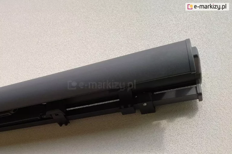 Markiza Palladio Selt w kolorze srebrzysty grafit z całkowicie zamknięta kaseta oraz widocznymi od spodu złożonymi ramionami i mocowaniem do ściany o jasnoszarej elewacji.