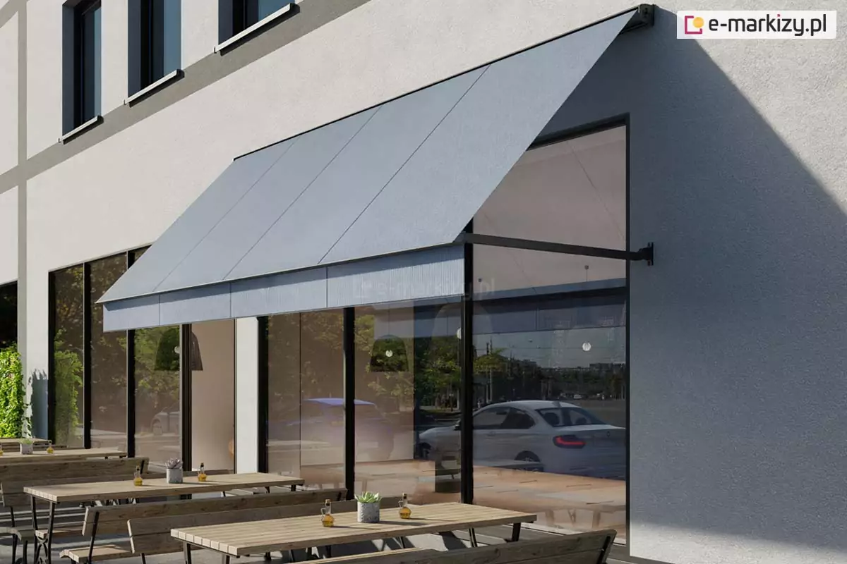 Wizualizacja zewnętrznego ogródka restauracyjnego lub kawiarnianego usytuowanego bezpośrednio przy nowoczesnym budynku o jasnej, tynkowanej elewacji. Nad dużymi witrynami lokalu zamontowana jest szeroka markiza fasadowa w kolorze jasnoszarym. Jest to model markizy z ramionami opadowymi, których punkty montażowe znajdują się po bokach okien, co pozwala na stabilne nachylenie poszycia pod kątem. Markiza jest w pełni rozwinięta, osłaniając wnętrze lokalu oraz część stolików przed słońcem. W witrynach odbija się ulica, biały samochód osobowy oraz zieleń miejska. Przed lokalem, na chodniku, ustawiono rzędy drewnianych stolików i ław o prostej konstrukcji z metalowymi stelażami. Na stolikach widoczne są drobne elementy dekoracyjne, takie jak małe doniczki z sukulentami oraz karafki z oliwą. Podłoże stanowi jasna nawierzchnia brukowa. Budynek charakteryzuje się regularnym rytmem okien na wyższych kondygnacjach, podkreślonych ciemniejszymi pasami elewacji. Oświetlenie wskazuje na słoneczne popołudnie, a cienie rzucane przez markizę i meble są wyraźne i krótkie.
