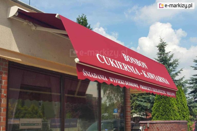 Zawieszona nad szeroką witryna sklepową markiza Allegro MOL o łamanym wysięgu z dodatkowym daszkiem osłonowym o białym kolorze. Na czerwonej tkaninie poszycia nadruk "BONBON CUKIERNIA-KAWIARNIA", na falowanej falbanie kolejny nadruk reklamowy "ŚNIADANIA WYPIEKI DOMOWE PRDUKTY EKOLOGICZNE SOKI KAWA". W tle za witryna widoczny niski ceglany murek oraz wysokie iglaki, a nad nimi błękitne niebo z kłębiastymi chmurami nad horyzontem.