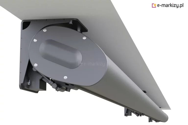 Zbliżenie na aluminiową kasetę markizy tarasowej w kolorze antracytowym (ciemnoszarym), zamontowaną pod sufitem lub wnęką balkonową. Na pierwszym planie widoczny jest boczny dekiel kasety o obłym, aerodynamicznym kształcie, przymocowany za pomocą czterech srebrnych śrub montażowych. Konstrukcja wsparta jest na solidnym, stalowym uchwycie montażowym przytwierdzonym pionowo do ściany i poziomo do stropu. Pod kasetą widoczny jest mechanizm przegubowy ramienia markizy wraz ze śrubami regulacyjnymi kąta nachylenia. Markiza Casablanca Aluprof jest w stanie całkowicie złożonym (zamkniętym), gdzie profil przedni idealnie przylega do obudowy, tworząc szczelną kasetę chroniącą poszycie materiałowe przed czynnikami atmosferycznymi. W tle widoczny jest fragment sufitu oraz dalsza część długiej konstrukcji markizy, co ukazuje powtarzalność uchwytów mocujących wzdłuż całej długości profilu.