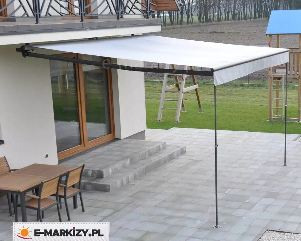 Markiza tarasowa Australia zainstalowana na ścianie nad wyjściem na taras z dwoma stopniami. W pełni rozwinięty wysięg markizy o szarym poszyciu wsparty został podporami PLUS (LUX) do markiz SELT. W tle widoczny trawnik z placem zabaw dla dzieci. Na tarasie wyłożonym betonowymi płytkami umieszczony jest także metalowy stół z drewnianym blatem i dopasowanymi do niego trzema krzesłami.