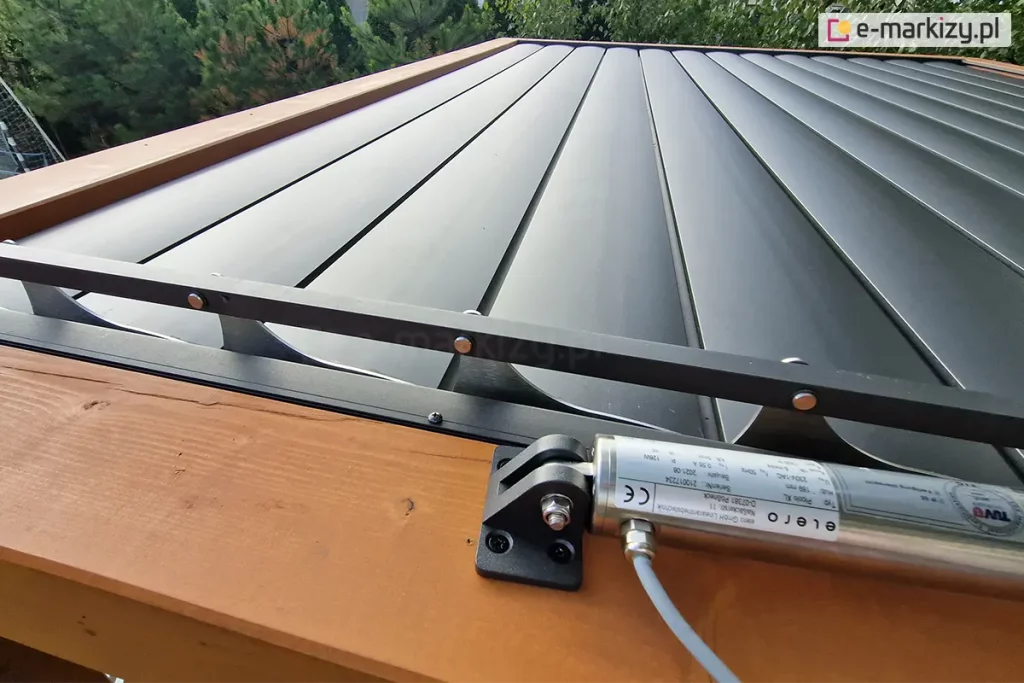 Zbliżenie mocowania silnika dachu lamelowego SB400 MD Selt do belki pergoli drewnianej. W tle widoczne zamknięte lamele dachu w kolorze antracytowym.