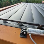 Zbliżenie mocowania silnika dachu lamelowego SB400 MD Selt do belki pergoli drewnianej. W tle widoczne zamknięte lamele dachu w kolorze antracytowym.