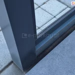 Mocowanie stałej ściany szklanej Fest do zadaszenia Lunaro. Pomiędzy podporami zainstalowane zostało okno w ramie. Pod zadaszeniem widoczny taras wyłożony betonowymi płytkami i kostką.