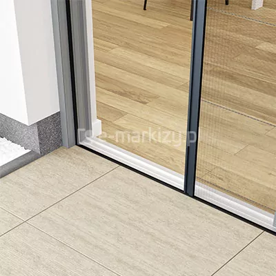 Moskitiera plisowana drzwiowa Fit Zag zamocowana na oknie przesuwnym z progiem HS tuż przy ramie okna na płytkach tarasowych o drewnopodobnym wzorze. W tle, w otwartym pomieszczeniu widoczna podłoga z drewnianych paneli.