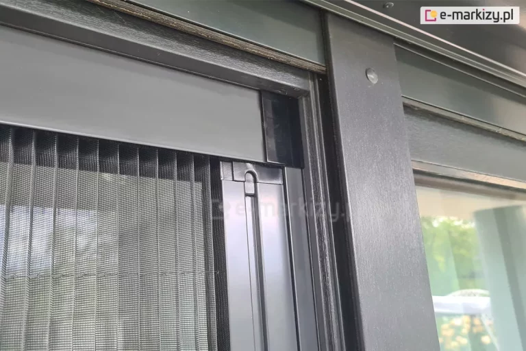 Zbliżenie narożnika moskitiery plisowanej Click Rol z czarnym łącznikiem profilu bocznego oraz górnego. W profilu górnym ukryta pozostaje gąsienica, która odpowiada za prawidłową pracę siatki w kolorze szarym.