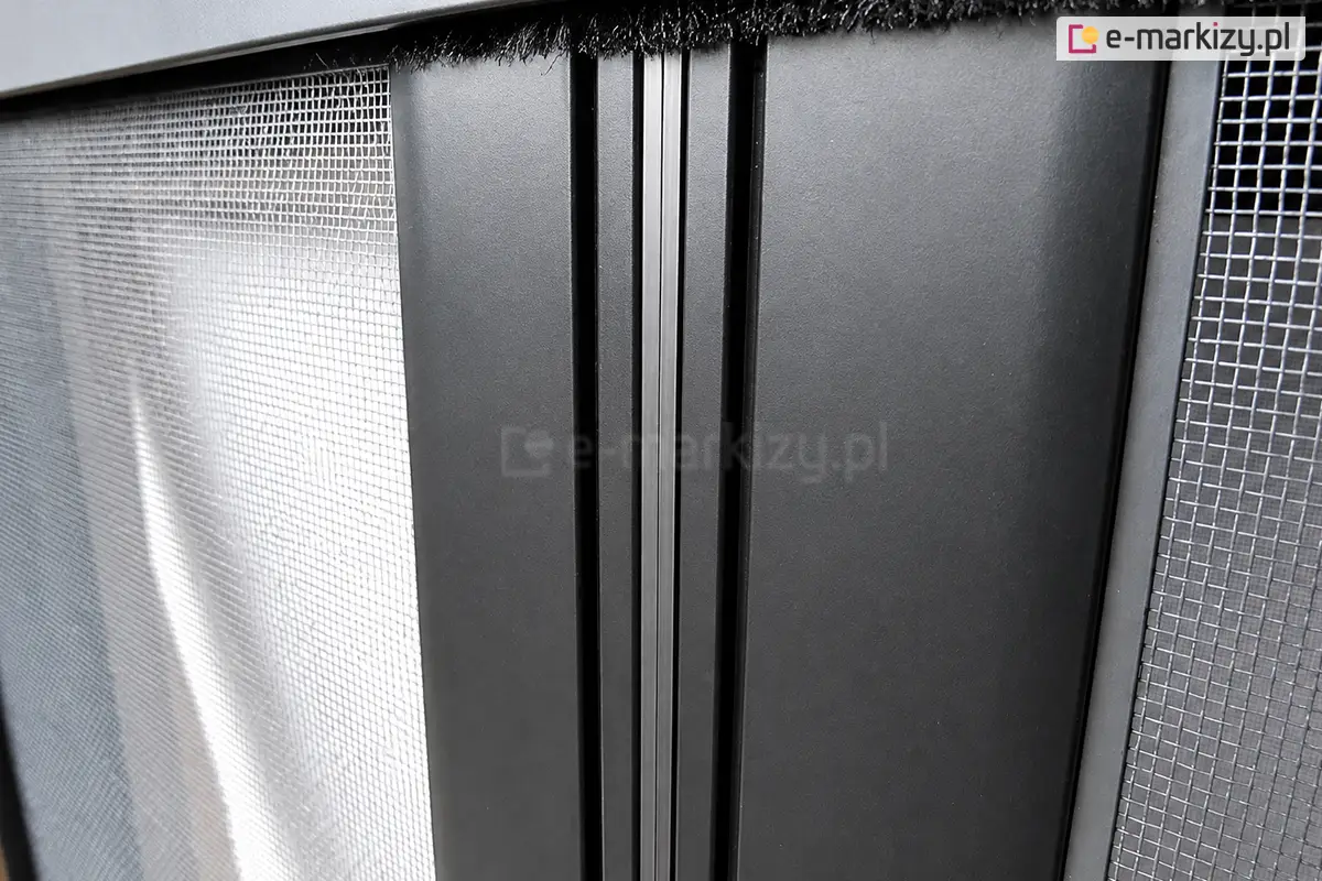 Zbliżenie magnetycznego domknięcia profili moskitiery rolowanej poziomej podwójnej w kolorze antracytu z widoczna w górnym profilu uszczelką szczotkową, która dodatkowo zabezpiecza pomieszczenie przed przedostawaniem się do wnętrza insektów.