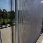 Wnęka okienna o białym tynku strukturalnym z oknem tarasowym w odcieniach antracytu i dopasowaną kolorystycznie moskitierą plisowaną Top Zag, o dwustronnym otwieraniu.