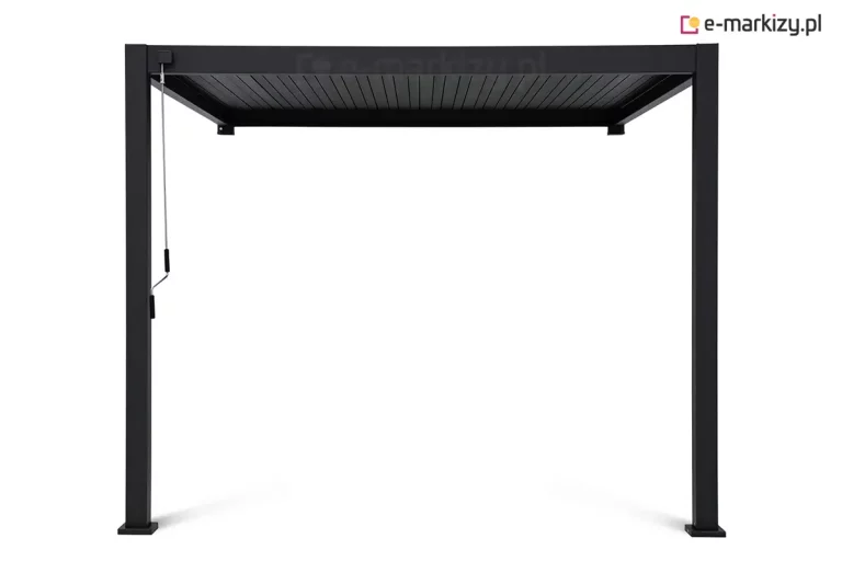 Antracytowa pergola bioklimatyczna Gloria w wersji przyściennej, przedstawiona od frontu na jasnym tle. Konstrukcja montowana jest bezpośrednio do elewacji budynku za pomocą dwóch punktów kotwiących widocznych na tylnej ramie, natomiast z przodu opiera się na dwóch pionowych słupach o kwadratowym przekroju, zakończonych stopami montażowymi. Zadaszenie składa się z systemu poziomych, ruchomych lameli aluminiowych, które w tej konfiguracji są całkowicie zamknięte, tworząc szczelną i płaską powierzchnię dachu. Po lewej stronie, przy przednim słupie, zamontowany jest pionowy drążek korbowy służący do ręcznej regulacji kąta nachylenia lameli. Całość charakteryzuje się nowoczesnym, minimalistycznym designem i matowym wykończeniem lakierowanej proszkowo powierzchni.