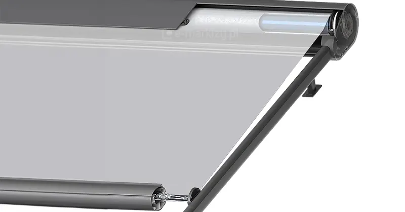 Renderowanie 3D w zbliżeniu prezentuje detaliczne rozwiązanie techniczne zastosowane w systemie osłony poziomej typu Veranda, koncentrując się na sposobie umiejscowienia napędu wewnątrz aluminiowej kasety. Grafika ukazuje fragment profilu kasety w przekroju, wewnątrz której widoczna jest rura nawojowa oraz zintegrowany z nią silnik elektryczny o cylindrycznym kształcie, umieszczony w osi obrotu wału. Obraz ilustruje również sposób wyprowadzenia tkaniny z kasety w stronę prowadnic bocznych oraz konstrukcję belki końcowej, która odpowiada za utrzymanie materiału w odpowiednim stopniu naprężenia. Całość grafiki, dzięki zastosowaniu efektu częściowej przezroczystości obudowy, pozwala na precyzyjne zrozumienie mechaniki działania osłony, pokazując zarówno schowany napęd, jak i system prowadzenia tkaniny, co jest kluczowe dla oceny trwałości i funkcjonalności tego typu zabezpieczenia przed nasłonecznieniem.