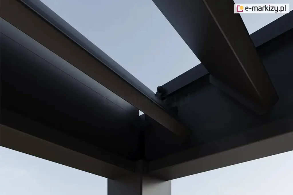 Zbliżenie na górny narożnik konstrukcji antracytowej pergoli lamelowej Marlo, ilustrujące mechanizm obrotowy lameli. Widoczne są dwa główne profile ramy łączące się pod kątem prostym, osadzone na pionowym słupie o kwadratowym przekroju. Wewnątrz ramy zamontowane są ruchome lamele o aerodynamicznym kształcie, które na zdjęciu znajdują się w pozycji otwartej, odsłaniając jasne niebo. Na krawędzi profilu bocznego widoczne są punkty mocowania oraz elementy mechaniczne odpowiedzialne za płynną zmianę kąta nachylenia piór. Konstrukcja charakteryzuje się matowym wykończeniem powierzchni oraz precyzyjnym spasowaniem elementów aluminiowych. Detal ten podkreśla techniczną stronę systemu bioklimatycznego, umożliwiającego regulację dopływu światła i cyrkulację powietrza pod zadaszeniem.