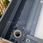 Zbliżenie połączenia rynny w belce przedniej zadaszenia Modes z rurą spustową ukrytą w nodze tego zadaszenia. Całość tworzy spójny system odprowadzania deszczówki z powierzchni poliwęglanu i zapewnia szczelną osłonę tarasu przed deszczem.